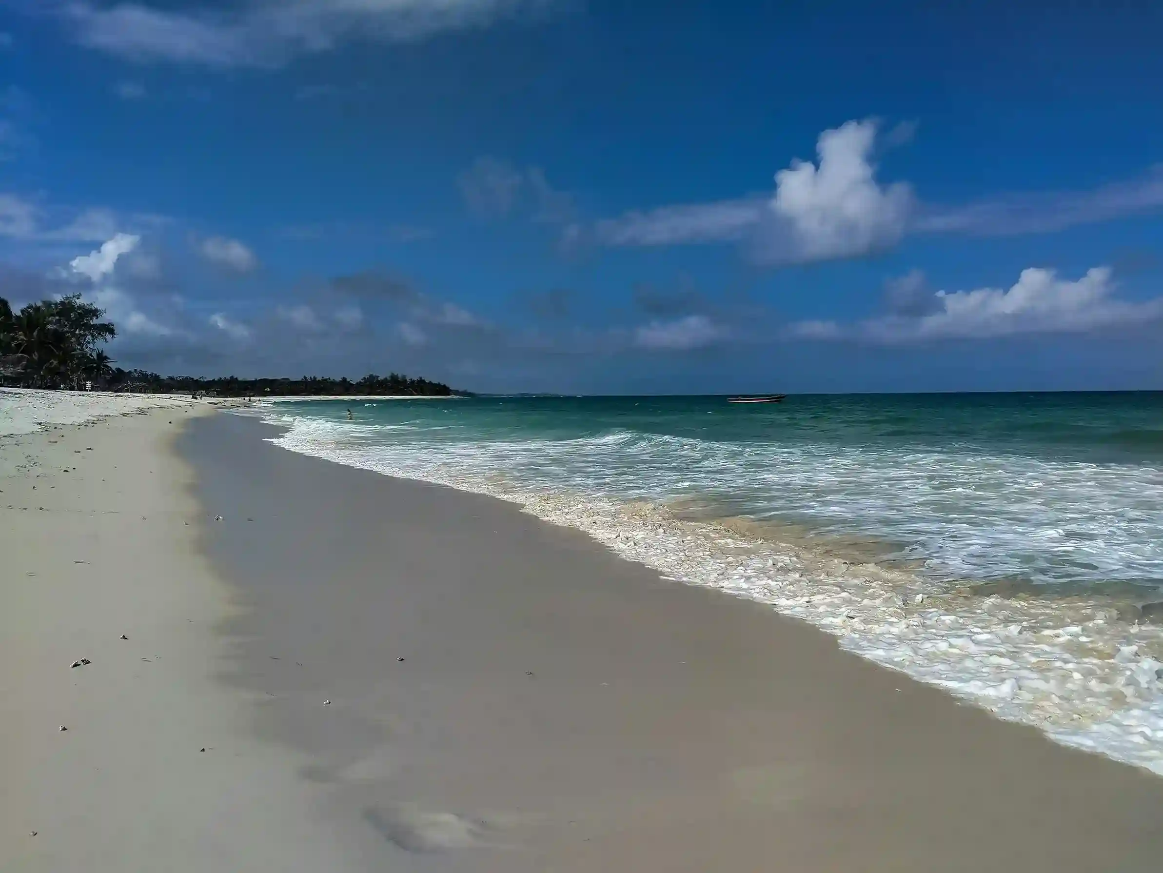White sandy beach and turquoise waters at Diani Beach with palm trees along the coast
